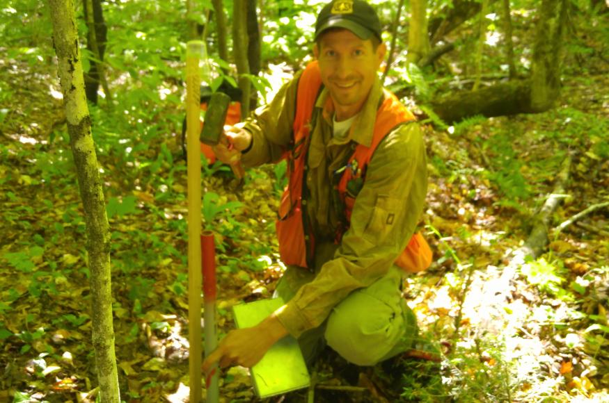 A researcher installs a marker for the center of a research plot.